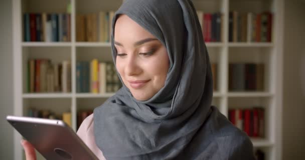 ヒジャーブでイスラム教徒の学生のクローズアップ肖像画は、ライブラリでアプリを推薦するタブレットの緑のクロマ画面を示しています. — ストック動画