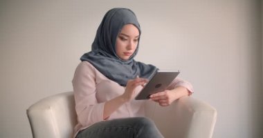 Başörtüsü müslüman iş kadını tablet ile özenle koltuk kameraya gülümsüyor özenli olmak ile çalışıyor.