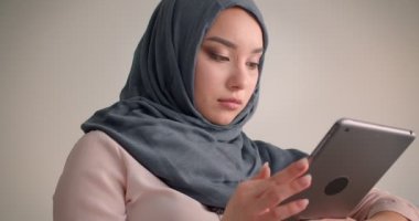 Başörtüsü takan Müslüman iş kadınının, koltukta çalışırken özenle tablete dalan yakın çekim.