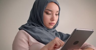 Başörtüsü takan Müslüman iş kadınının tabletle çalışırken çekilen yakın çekimi ofiste sakince kameraya gülümsüyor.