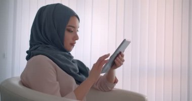 Başörtüsü müslüman iş kadını tablet ile çalışan profil çekimi ofiste neşeli olmak kameraya gülümsüyor.