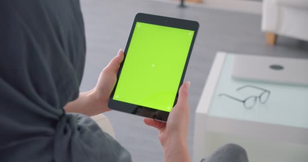 Мусульманская предпринимательница в хиджабе держит планшет с зеленым хроматическим экраном часы в его сидя в офисе . — стоковое видео