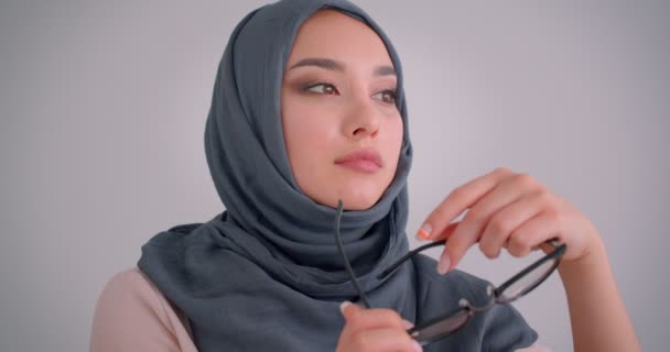 Close-up portrait of dreamy muslim businesswoman in hijab plays with her eyeglasses and watches calmly into camera. — Stock Video