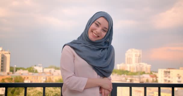 Portré a muzulmán hallgató hidzsáb mosolyogva kamera állt az erkélyen, nagy város kilátás. — Stock videók