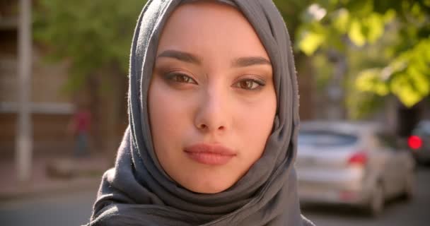 Portrait of Muslim student in hijab watching calm and modestly into camera standing on green city street . — Stok Video