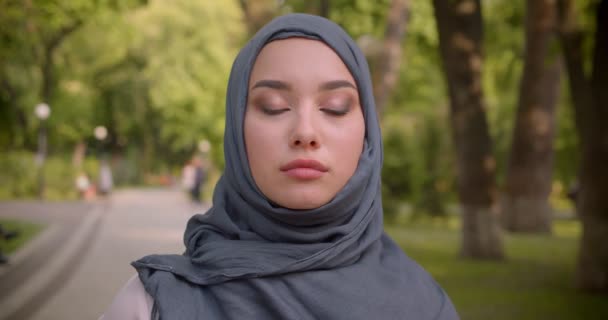 Retrato de una mujer musulmana en hijab mirando seriamente a la cámara caminando por el parque . — Vídeos de Stock
