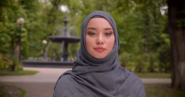 Retrato de una mujer musulmana en hijab mirando seriamente a la cámara de pie frente a la fuente . — Vídeos de Stock