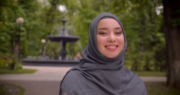 Çeşmenin önünde duran kameraya gülümseyen türbanlı rüya gibi müslüman öğrencinin portresi. — Stok video
