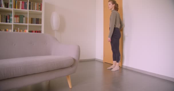 Tendre caucasienne fille entre dans la chambre et se trouve sur le canapé étirement et la lecture d'un livre simultanément . — Video