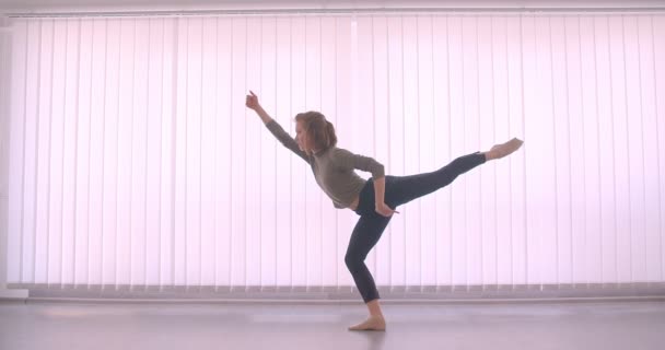 Anbud kaukasiska professionell ballerina dansar charmigt och göra tricks i ljus Studio på lameller bakgrund. — Stockvideo