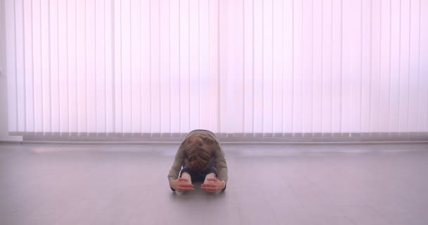 Tierna bailarina profesional caucásica calentando sus piernas en estudio de luz sobre fondo de persianas . — Vídeo de stock