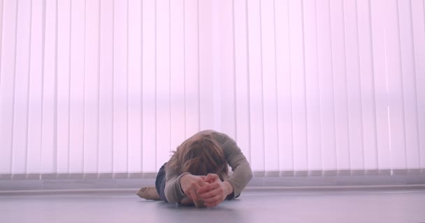 Tierna bailarina profesional caucásica calentando haciendo leg-split en estudio de luz sobre fondo de persianas . — Vídeo de stock