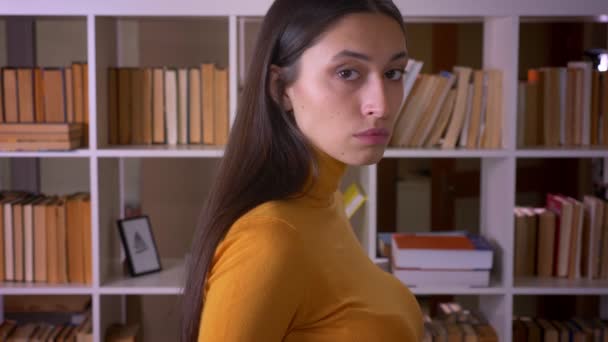 Porträt einer stilvollen brünetten Lehrerin wendet sich der Kamera zu und schaut in der Bibliothek aufmerksam hinein. — Stockvideo