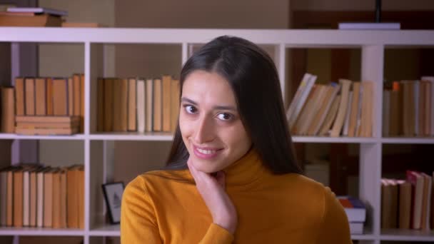 Ritratto di carina bruna insegnante di sesso femminile che posa timidamente nella fotocamera gioiosa per la biblioteca . — Video Stock