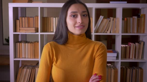 Portrait of brunette female teacher flirtingly blinking into camera being cute and beautiful at the library. — Stock Video