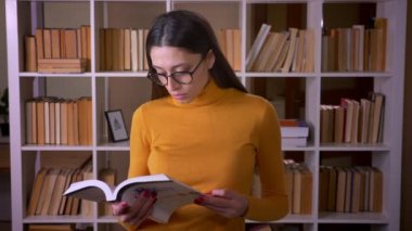 Kütüphanede kitap okuyan gözlük güzel esmer öğretmen Portresi kamera ve gülümsüyor döner.