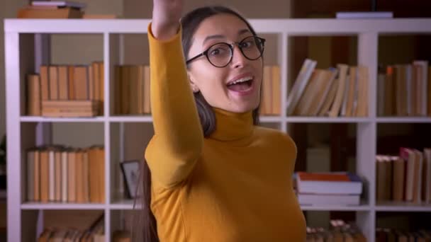 Glücklich und erfreut brünette Lehrerin gestikuliert Daumen-hoch-Zeichen zu zeigen, wie und Respekt in der Bibliothek. — Stockvideo