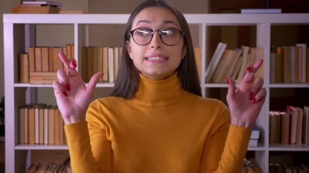 Portret stylowej kobiety brunetka nauczyciel modląc się z przekreślone palce nadzieję na szczęście w bibliotece. — Wideo stockowe