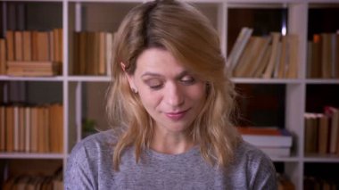 Orta yaşlı sarışın öğretmen kütüphanede son derece utanan kameraya utangaç bir şekilde gülümsüyor.