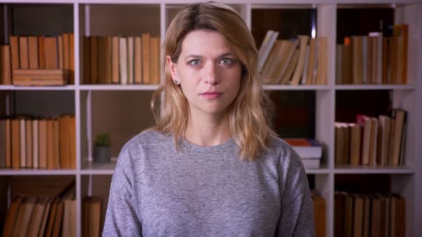 Portrait d'un professeur blond d'âge moyen regardant calmement et intensément dans la caméra sur fond de bibliothèque . — Video