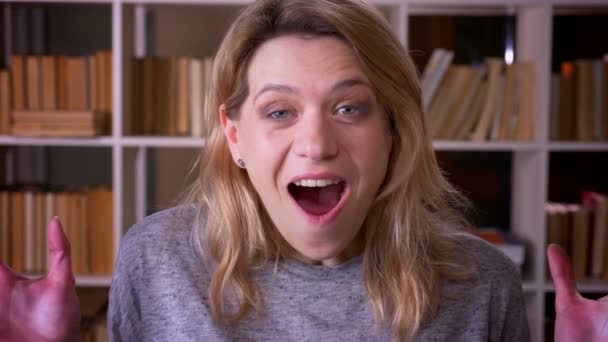 Учительница блондинки средних лет демонстрирует сильное развлечение и счастье в камерах в бухтах лица руками в библиотеке . — стоковое видео
