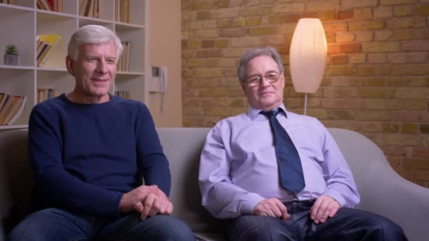 Portrait of old male friends watching TV together get extremely happy and delighted raising hands in gladness. — Stock Video