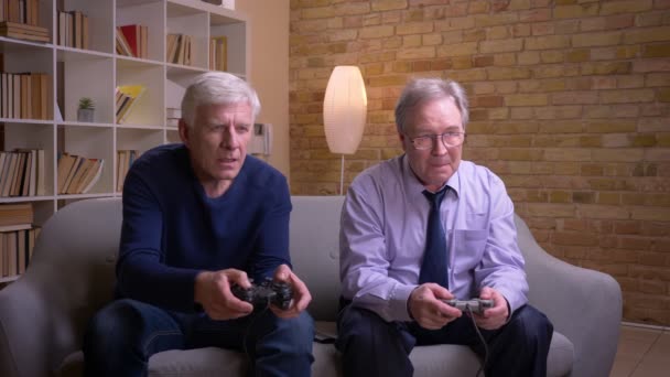เพื่อนชายผู้สูงอายุเล่นวิดีโอเกมร่วมกับจอยสติ๊กและคอนโซลเกมสูญเสียและตกใจ . — วีดีโอสต็อก