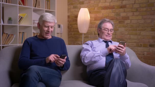 Retrato de amigos varones mayores sentados en silencio cada uno en su propio teléfono inteligente siendo absorbido y ocupado . — Vídeo de stock