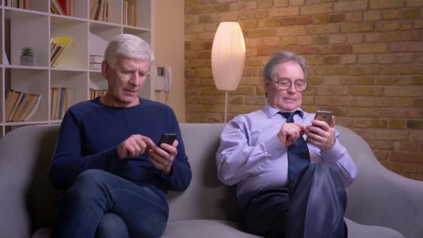 Portrait d'amis masculins seniors montrant les smartphones les uns aux autres et riant joyeusement . — Video