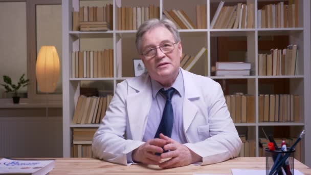 Interview du médecin principal en blouse blanche parlant à la caméra sur fond de rayonnages de livres . — Video