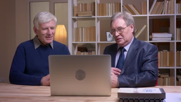 Portret van oude zakenlieden die samen aan tafel werken met laptop en het project serieus bespreken. — Stockvideo