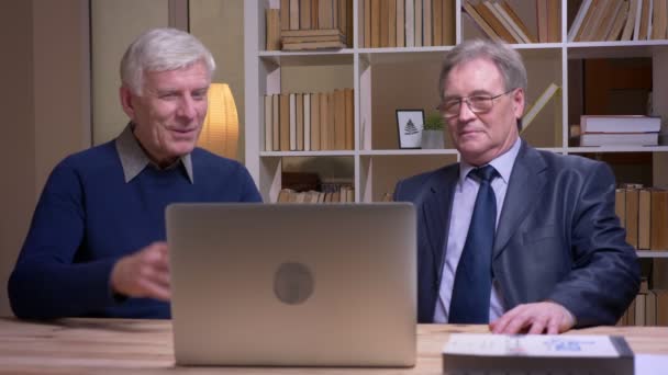 Retrato de viejos empresarios trabajando con laptop y discutiendo alegremente el proyecto . — Vídeos de Stock