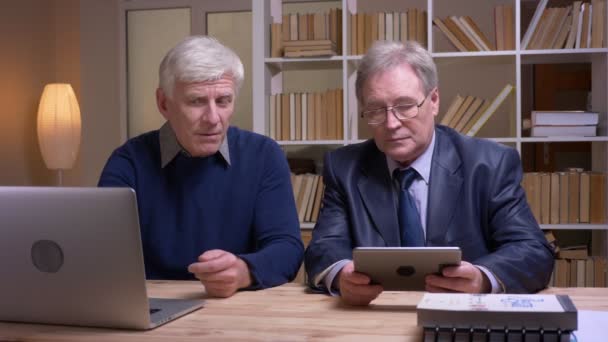 Retrato de viejos empresarios que trabajan junto con el ordenador portátil y la tableta discutiendo activamente el proyecto . — Vídeos de Stock