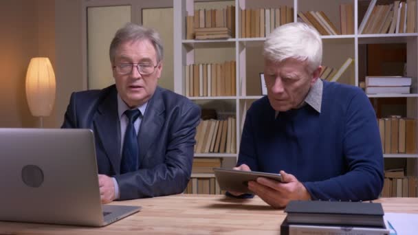 Portrait of old businessmen cooperating with laptop and tablet discussing seriously the future project. — Stock Video