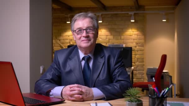 Portrait of senior man in formal costume sitting in front of laptop and smiling into camera being positive in office. — Stock Video