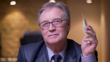 Resmi kostüm üst düzey işadamı portresi kamera içine mutlu ve ofiste memnun olmak para paketi gösterir.