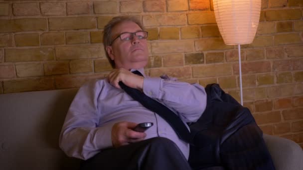 Porträt eines Geschäftsmannes im Kostüm, der nach einem anstrengenden Arbeitstag entspannt vor dem Fernseher sitzt und die Krawatte lockert. — Stockvideo
