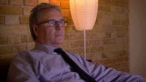 Portrait of senior businessman in costume chills out in front of TV after hard working day being attentive and amused. — Stock Video