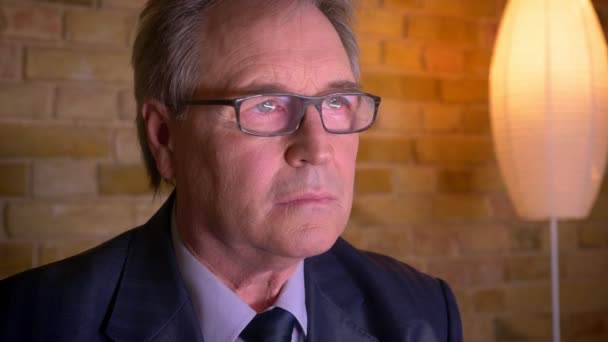 Portrait of senior businessman in costume and glasses watching news on TV being serious and concentrated. — Stock Video