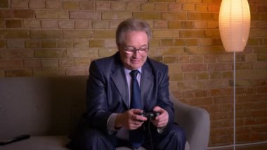 Tv joystick ile video oyunu oynayan kostüm kıdemli adam kaybeder ve evde üzgün olur.