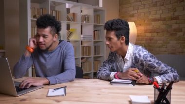 Birlikte işbirliği yapan Afrikalı-Amerikalı ve Hintli erkek öğrencilerin yakın çekim çekimleri. Biri dizüstü bilgisayarda yazarken diğeri not alıyor.