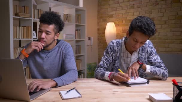 Gros plan sur des étudiants afro-américains et indiens travaillant ensemble sur un projet. L'un tape sur l'ordinateur portable tandis qu'un autre prend des notes — Video