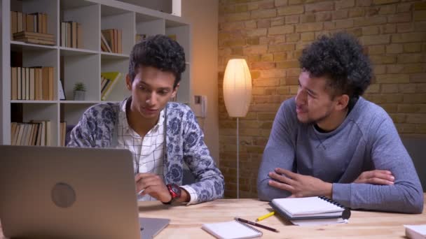 Närbild shoot av afroamerikanska och indiska manliga studenter diskuterar ett projekt tillsammans med på den bärbara datorn och med anteckningar — Stockvideo