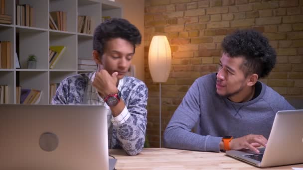 Sesión de primer plano de los estudiantes varones indios y afroamericanos que usan las computadoras portátiles y estudian en línea. Uno está pidiendo consejo a otro — Vídeo de stock