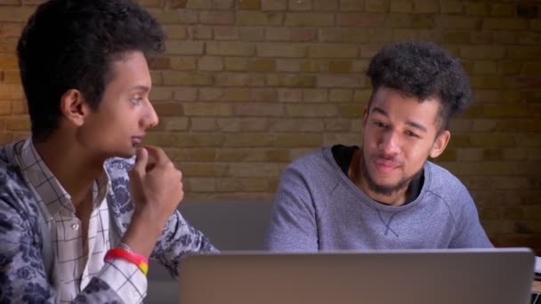 Closeup lő a fiatal indiai és afro-amerikai fiatal férfi barátai néz egy filmet a laptop megbeszélése izgalmat ül bent — Stock videók