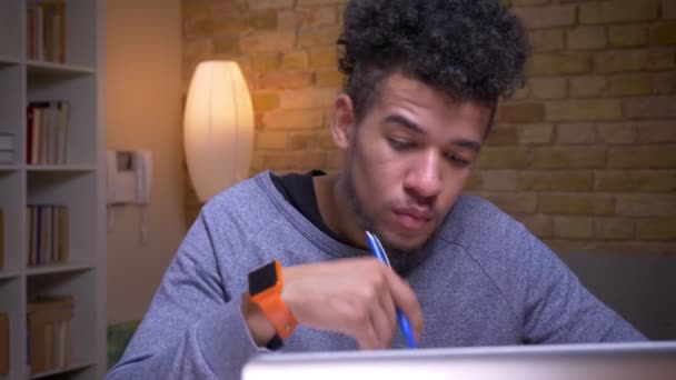 Close-up shoot by camera verhuizen van Afro-Amerikaanse naar Indiase mannelijke studenten met behulp van de laptops en leren Online zittend binnen in de bibliotheek samen — Stockvideo