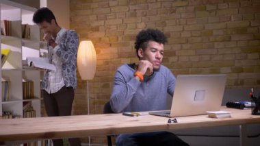 Üniversite kütüphanesinde birlikte okuyan etnik çeşitlilikte iki öğrencinin yakın çekim çekimleri. Hintli adam arka planda kitap okurken dizüstü bilgisayar kullanarak Afrikalı-Amerikalı erkek