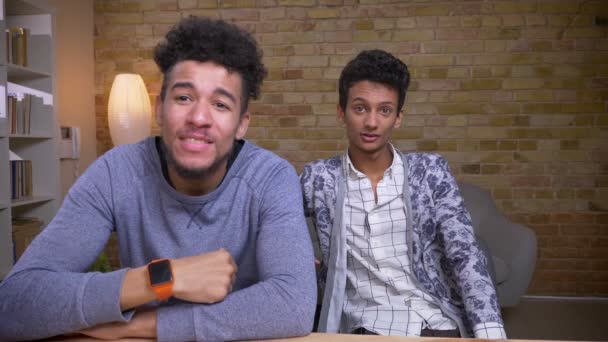 Closeup shoot of two young african american and indian male friends and bloggers streaming live talking on camera cheerfully indoors — Stock Video