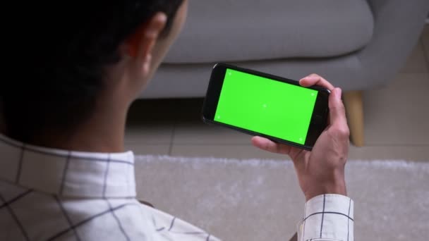 Primo piano vista posteriore ripresa di maschio avendo una videochiamata e gesticolando tenendo in mano un telefono con schermo chiave croma verde all'interno in appartamento — Video Stock