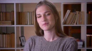 Kapalı üniversite kütüphanesinde utangaçlık ile gülümseyen kamera bakarak genç sevimli çekici kız öğrencinin Closeup portre